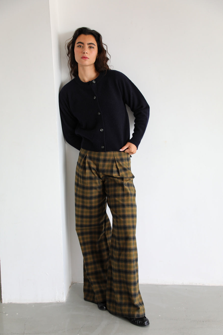 Full-length view of the navy wool Modern Buttons Knit Sweater with button-down front, worn with the wide-leg pleated Square Detail Pants Grey in grey and brown check cotton.