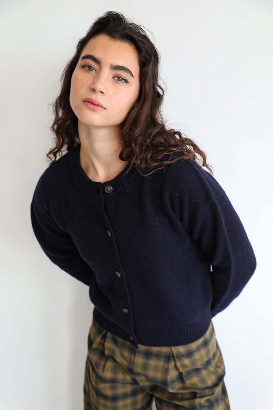 Close-up of the Modern Buttons Knit Sweater Navy, a 100% wool knit with round neck, button-down front and soft textured finish, worn with the grey and brown check Square Detail Pants.