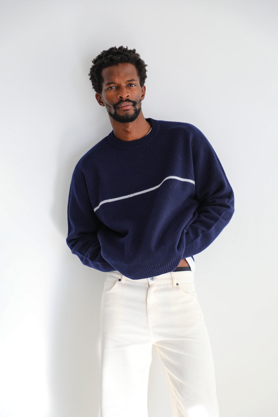 Close-up of the Line Round Knit Sweater Dark Blue: 100% wool knit with round neckline, ribbed hem and a white line across the chest, worn with the white cotton Corduroy Wide Comfy Pants.