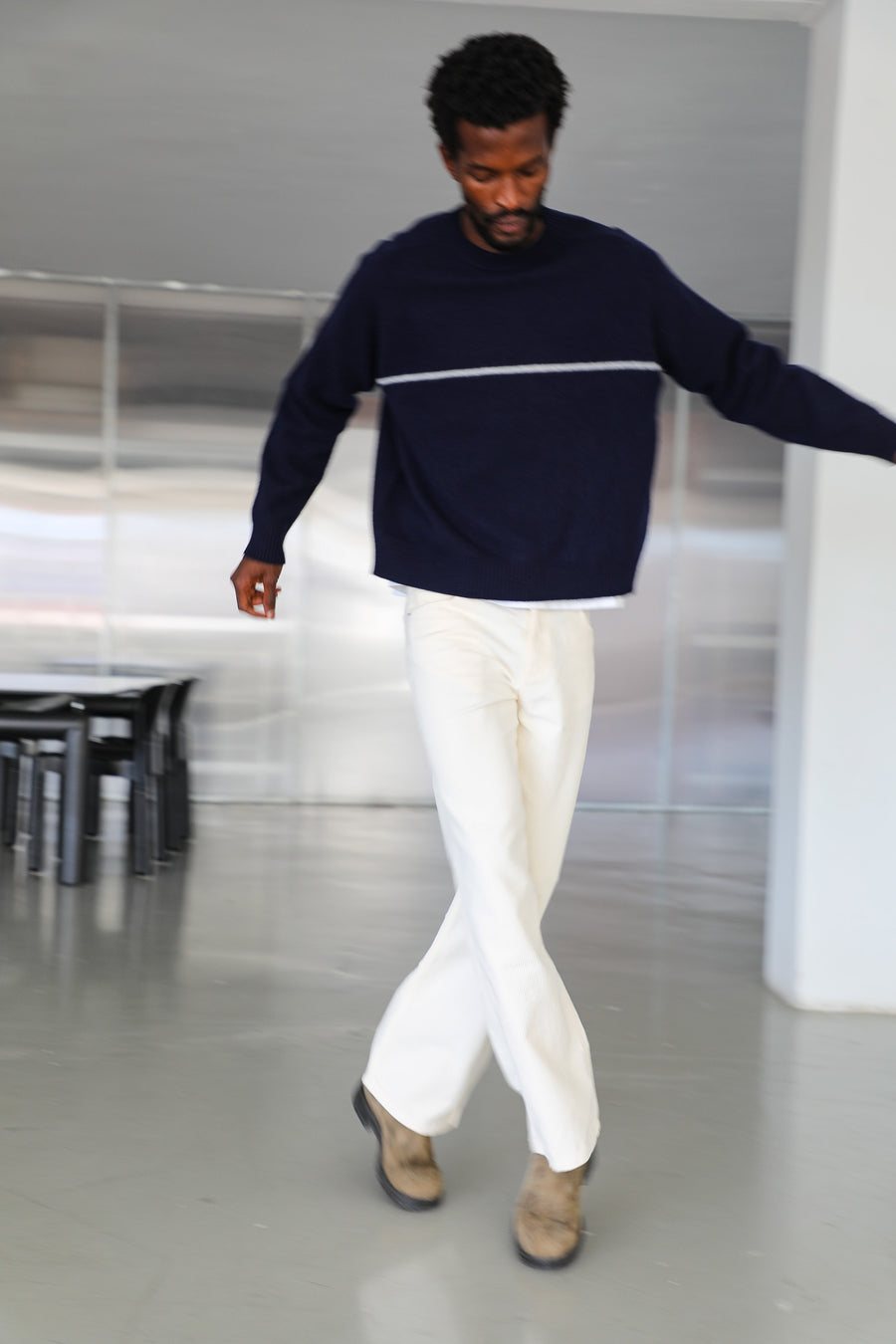 Model in motion wearing the dark blue wool Line Round Knit Sweater with its white contrast line and dropped shoulders, and the Corduroy Wide Comfy Pants White, relaxed wide-leg cotton corduroy trousers.