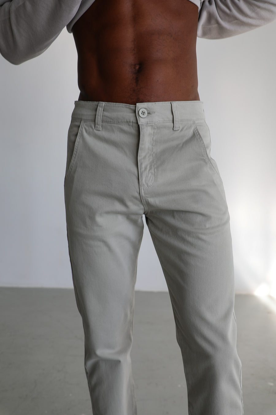 Waist detail of the Button Comfy Pants Green in 100% cotton: mother-of-pearl front button, belt loops, clean waistband with no elastic and slant pockets, under the light grey cotton Polo Sweater.